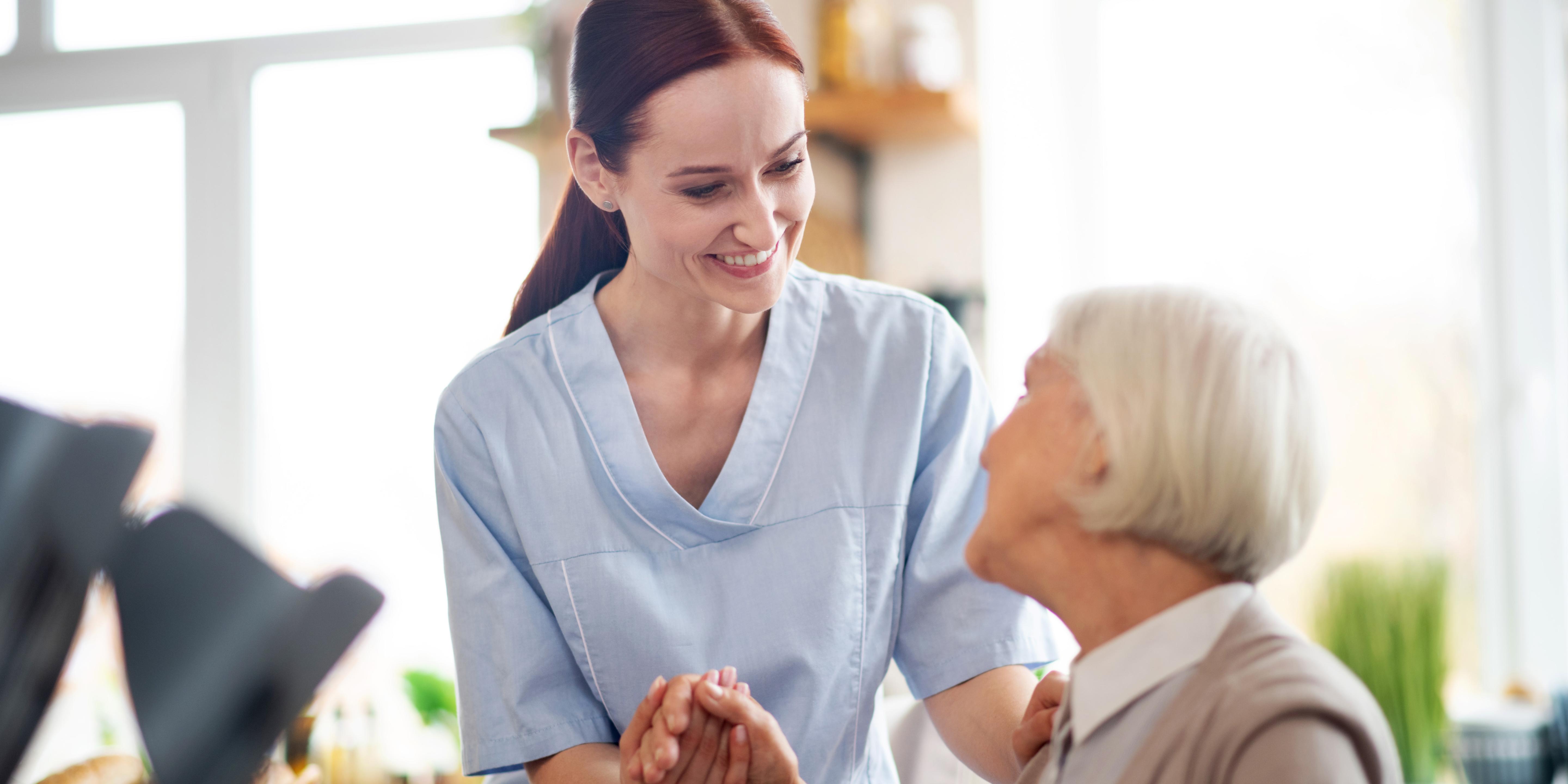 a caregiver in scrubs giving a hand to an elderly woman